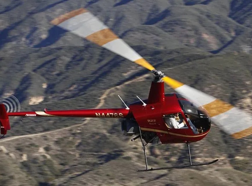 Robinson R-22 Beta II two-seat piston helicopter in flight over mountainous terrain
